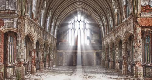 A dilapidated church interior with tall arches, broken windows, and beams of light illuminating the dusty space.