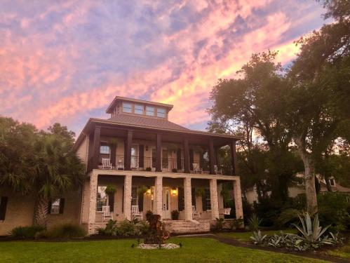 A charming two-story house with a porch, surrounded by greenery, under a colorful sunset sky.