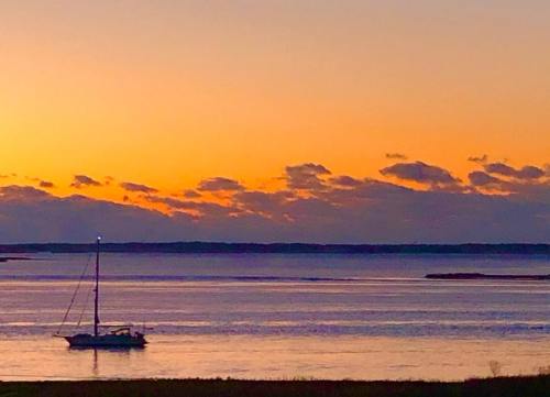 A sailboat on calm waters at sunset, with vibrant orange and purple clouds in the sky.