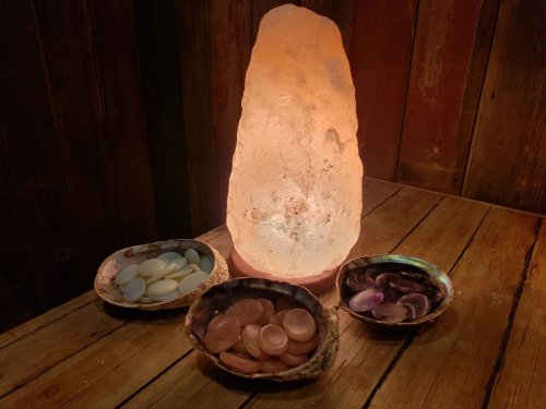 A glowing salt lamp surrounded by three bowls of colorful polished stones on a wooden surface.