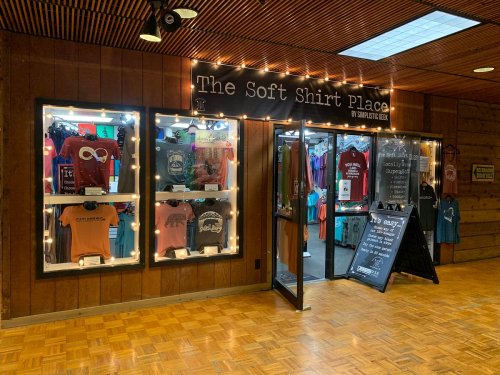 A storefront with illuminated displays showcasing colorful t-shirts and a chalkboard sign outside.