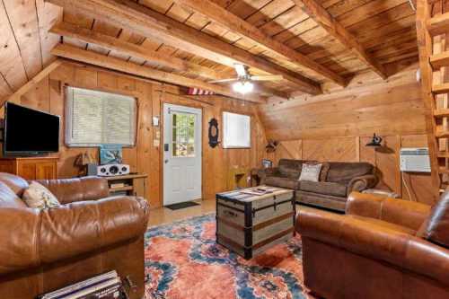 Cozy wooden cabin interior with leather sofas, a coffee table, and a door leading outside. Warm, rustic decor.