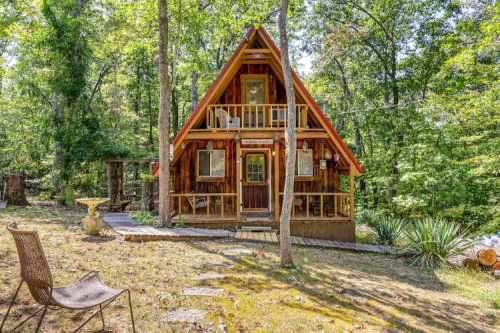 A charming A-frame cabin nestled in a wooded area, surrounded by trees and a small stone pathway.