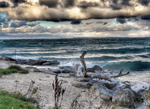 Waves crash against rocky shore under a dramatic sky with clouds, creating a serene coastal scene.