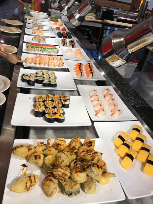 A variety of sushi and sashimi displayed on white plates at a buffet, including rolls, nigiri, and tempura.