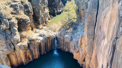 Aerial view of a rocky canyon with a waterfall cascading into a deep blue pool surrounded by greenery.