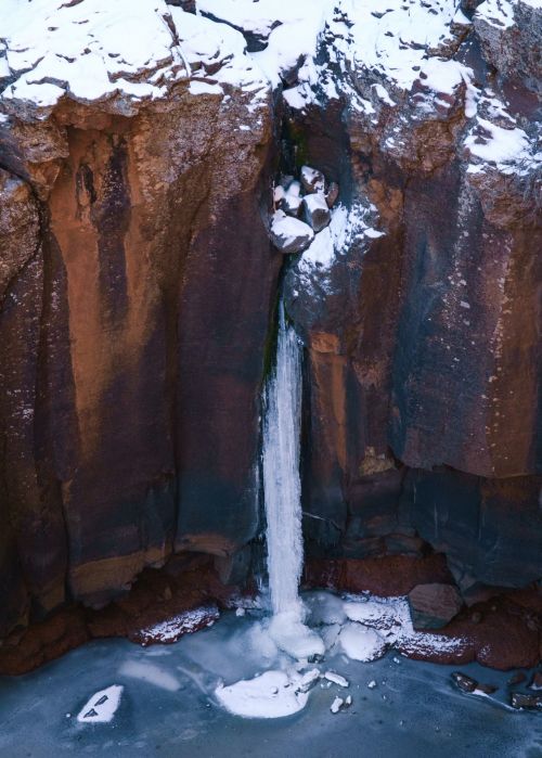 A frozen waterfall cascading down rocky cliffs, surrounded by snow and ice.