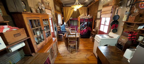 Cozy rustic interior of a cabin with wooden furniture, a kitchenette, and a bunk bed, featuring warm lighting and decor.