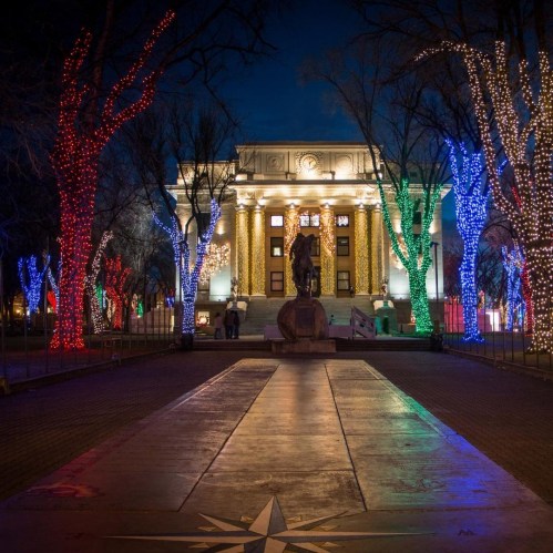 A beautifully lit building at night, surrounded by colorful trees adorned with festive lights.