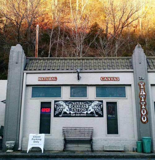 A tattoo shop named "Natural Canvas Tattoo" with an open sign, located in a mountainous area.