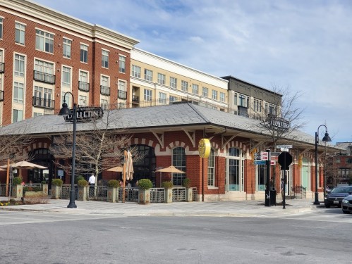A brick building with outdoor seating, part of a mixed-use development, under a clear blue sky.