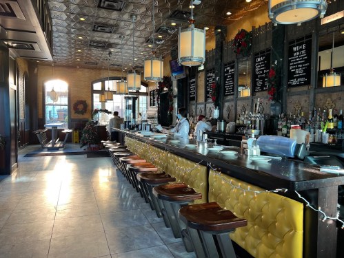 A stylish bar with yellow seating, festive decorations, and a well-stocked counter in a warm, inviting atmosphere.