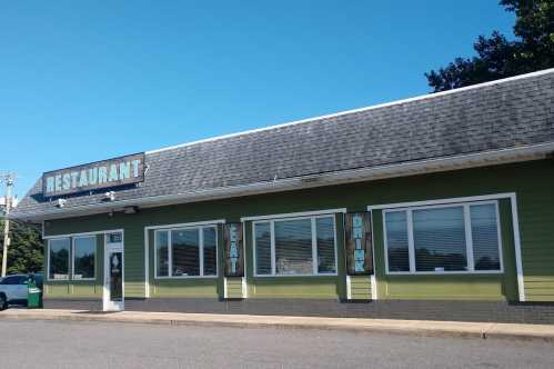 A green restaurant building with large windows and a sign that reads "RESTAURANT" against a clear blue sky.