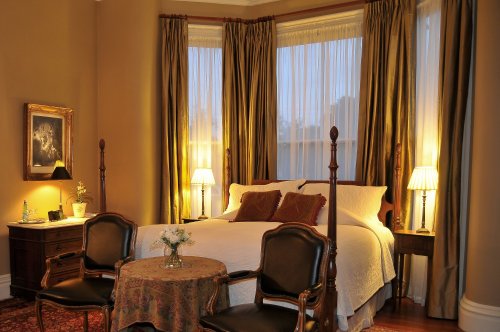 Cozy bedroom with a large bed, elegant curtains, two chairs, and warm lighting from bedside lamps.