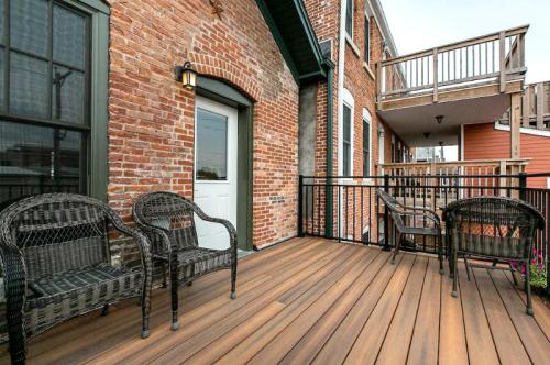 A cozy balcony with wicker chairs, wooden flooring, and brick walls, featuring a door and a view of nearby buildings.
