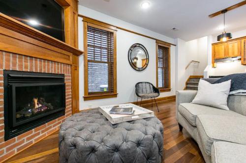 Cozy living room featuring a fireplace, tufted ottoman, and modern decor with wooden accents and large windows.