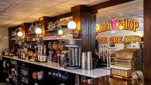 A vintage soda shop counter with ice cream machines, colorful syrups, and a decorative sign.