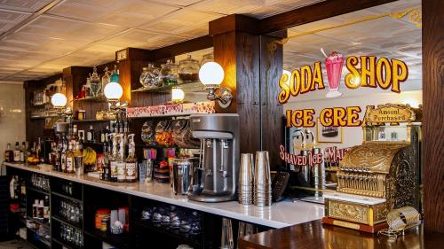 A vintage soda shop counter with ice cream machines, colorful syrups, and a decorative sign.