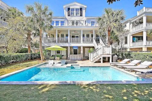A spacious backyard with a pool, lounge chairs, and a large house surrounded by palm trees under a clear blue sky.