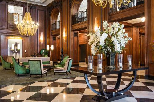 Elegant hotel lobby featuring wooden walls, ornate chandeliers, green seating, and a floral centerpiece on a table.