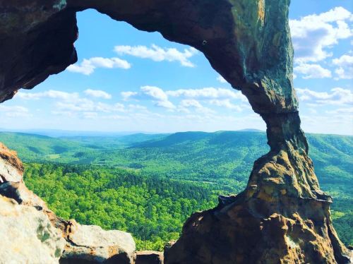 A scenic view of lush green mountains and blue skies framed by a natural rock arch.