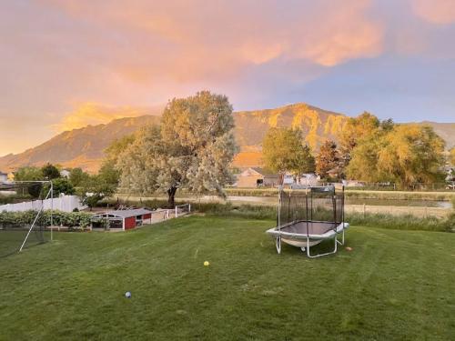 A scenic backyard at sunset, featuring a trampoline, green lawn, and mountains in the background.