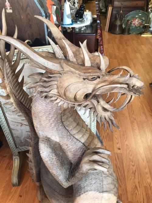 A detailed wooden dragon sculpture with intricate scales and fierce expression, displayed in a rustic setting.