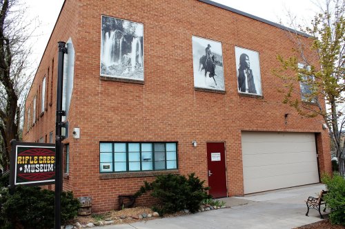 Exterior of the Rifle Creek Museum featuring large black-and-white photos on a brick building and a sign in front.
