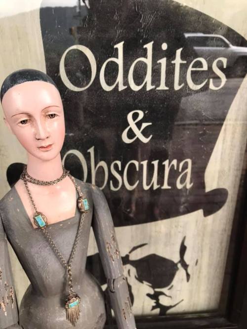 A vintage mannequin with a necklace stands in front of a sign that reads "Oddities & Obscura."