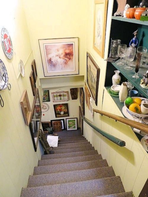 A staircase leading down, lined with framed art and decorative items on the walls and shelves.