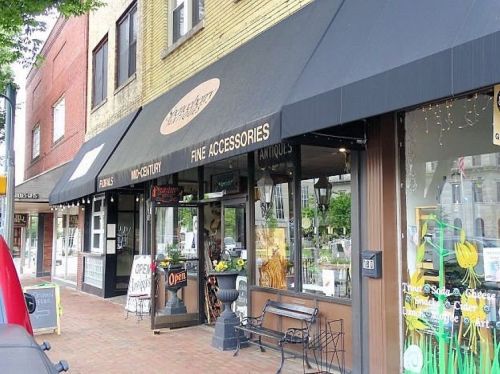 A street view of a shop with an awning labeled "Fine Accessories," featuring a display of various items in the window.