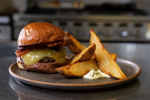 A juicy cheeseburger with bacon on a bun, served with crispy potato wedges and a side of dipping sauce.