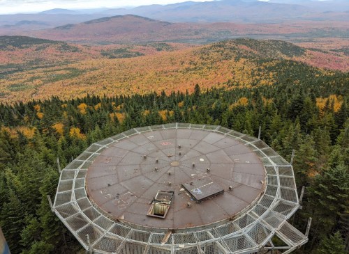 Aerial view of a circular observation platform surrounded by vibrant autumn foliage and distant mountains.