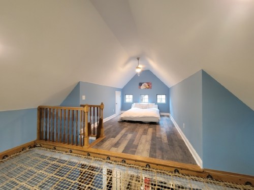 Cozy attic bedroom with blue walls, wooden flooring, and a bed under a sloped ceiling.