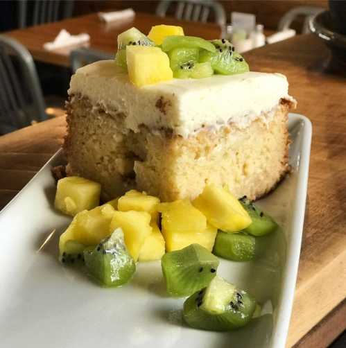 A slice of cake topped with cream and fresh fruit, including pineapple and kiwi, served on a white plate.