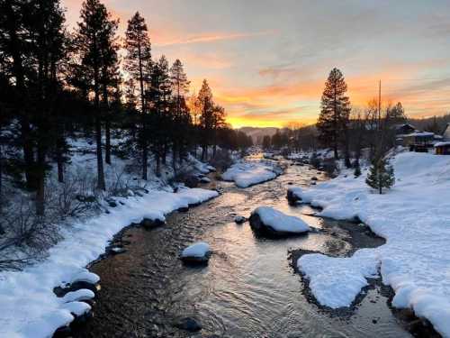 A serene winter landscape featuring a snow-covered river at sunset, surrounded by trees and rocky outcrops.