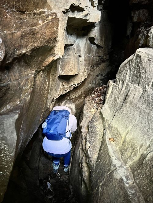 A person with a backpack navigating through a narrow rocky crevice in a cave or canyon.