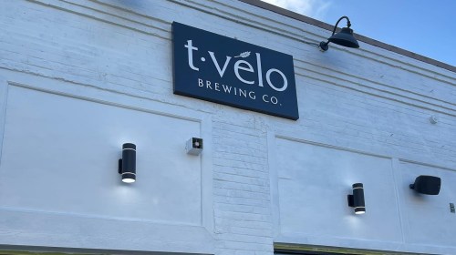 Sign for t. velo Brewing Co. on a white building with modern lighting fixtures. Clear blue sky above.