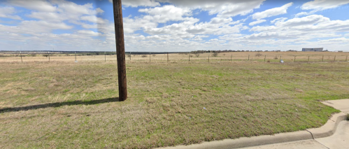 A wide open field with a fence, a utility pole, and a cloudy sky in the background.