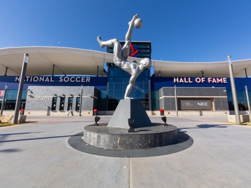 A silver soccer player statue in front of the National Soccer Hall of Fame building.
