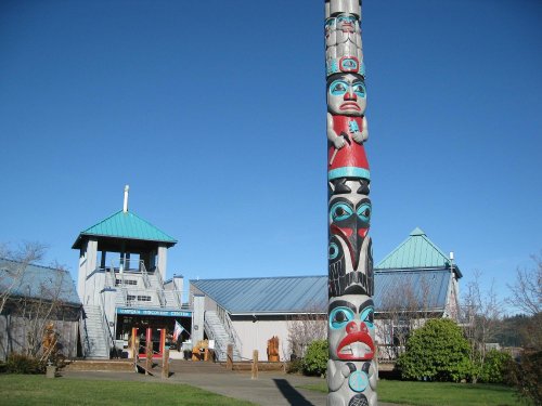 A colorful totem pole stands in front of a building with a blue roof and clear blue sky in the background.