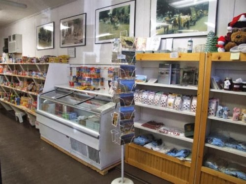 Interior of a small store featuring shelves of snacks, a freezer, and a display of postcards and souvenirs.
