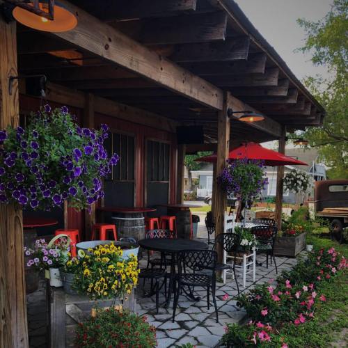 Charming outdoor café with colorful flowers, hanging plants, and patio seating under a wooden awning.