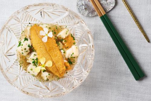 A delicate dish featuring sea urchin on a bed of creamy sauce, garnished with herbs and edible flowers, served in a crystal bowl.