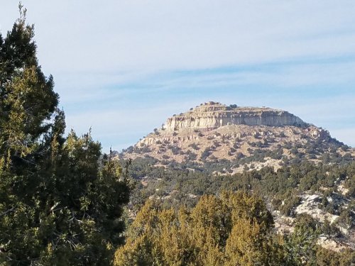 A rocky plateau rises above a forested landscape under a clear blue sky.
