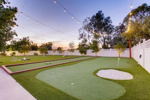 A backyard mini-golf area with artificial turf, a sand trap, and string lights against a sunset sky.