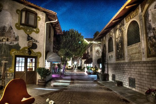 Charming cobblestone street lined with colorful buildings and murals, illuminated by soft evening lights.