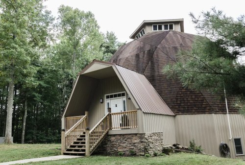 A unique dome-shaped building with a wooden deck, surrounded by trees and greenery.