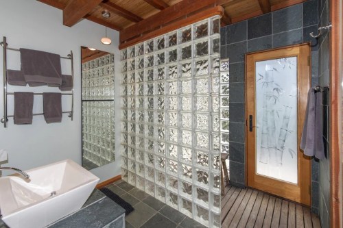 Modern bathroom featuring a glass block shower, wooden door, and sleek sink with gray towels on a rack.