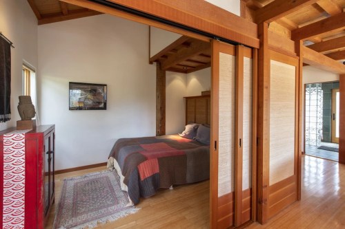 A cozy bedroom with wooden sliding doors, a patterned bedspread, and natural light streaming in from a nearby window.